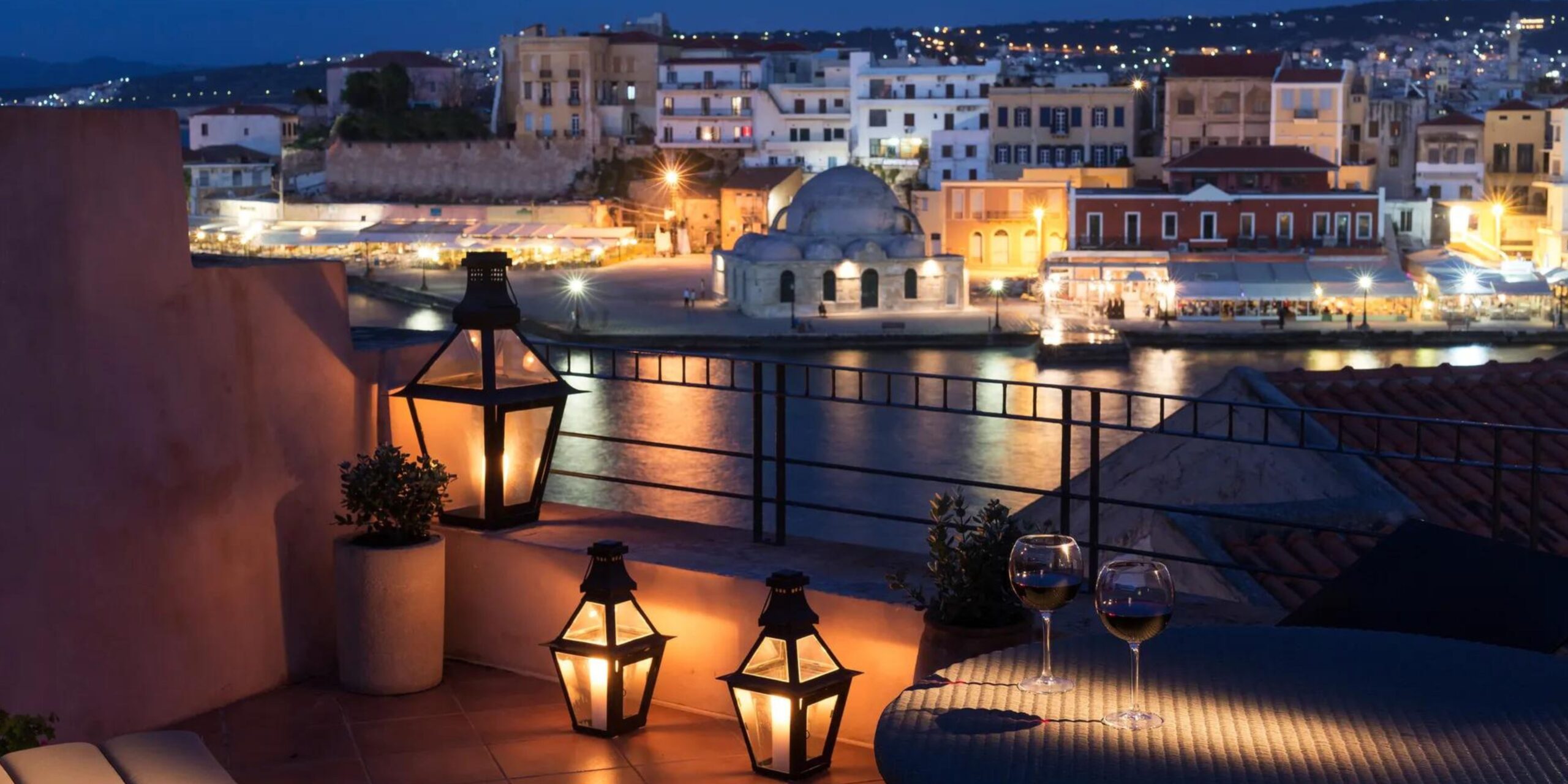 Evening view from a balcony with lanterns, overlooking a coastal town and waterfront.