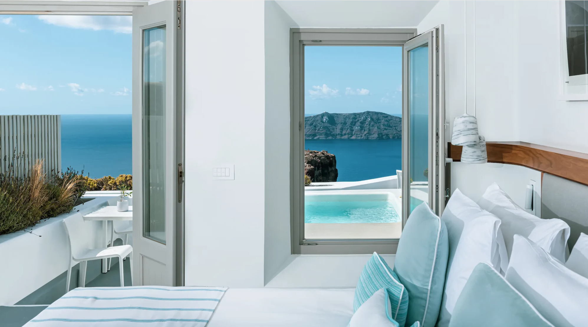 View from a bedroom through open doors to a private balcony with a pool overlooking the sea and a distant island.