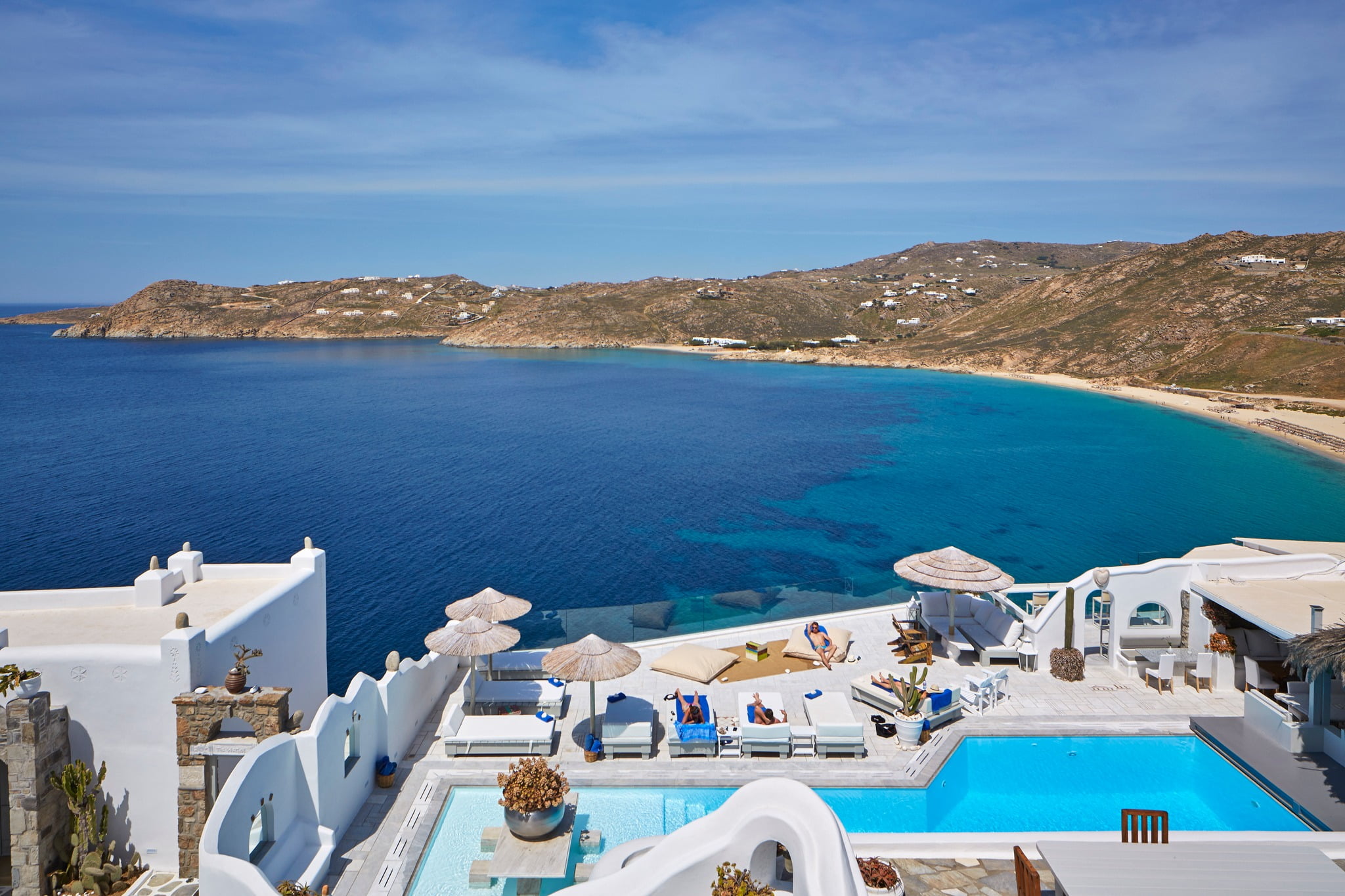 Pool stretches towards the Aegean Sea, lined with comfy sun loungers under sunshades. 