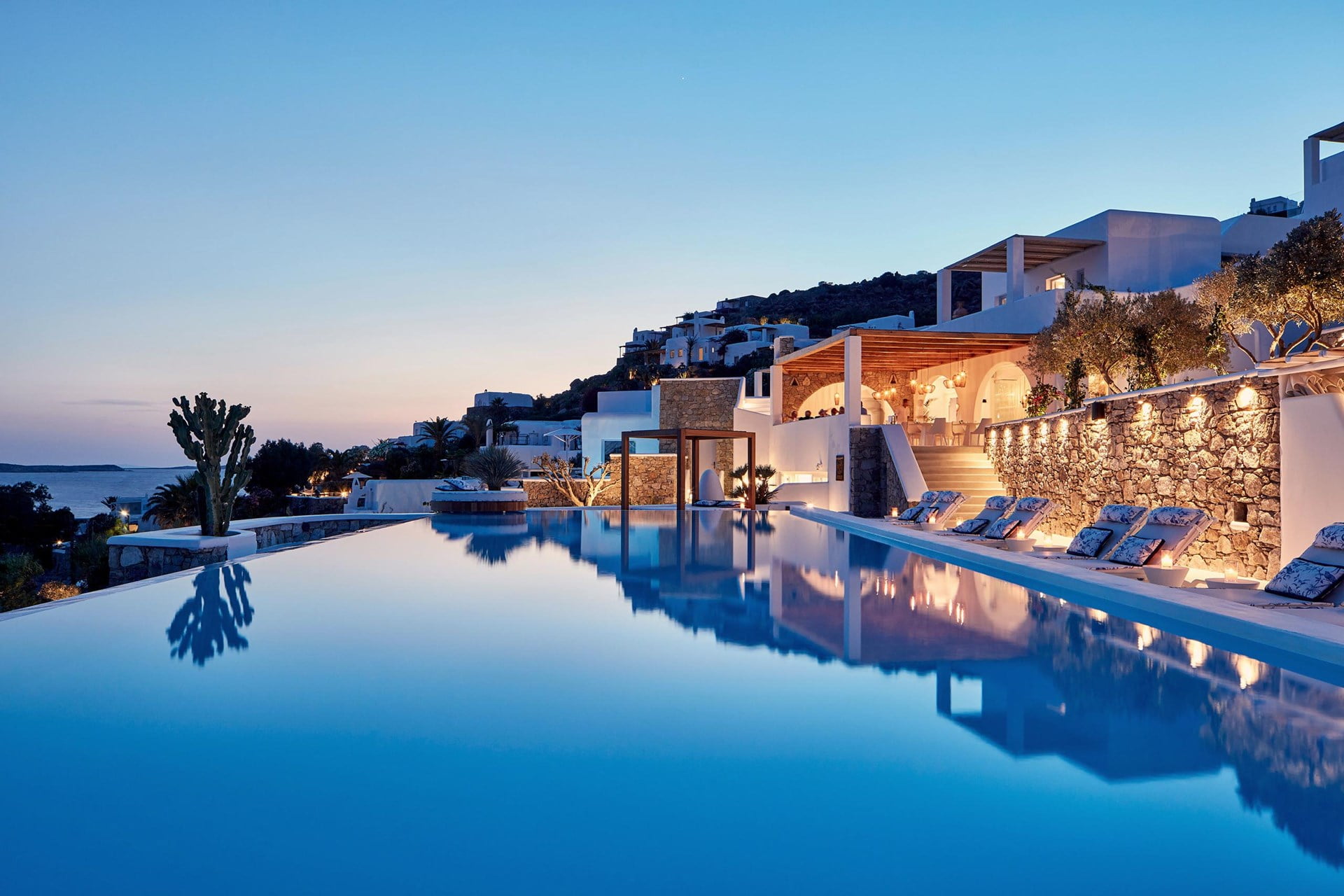 Nighttime view of Katikies hotel in Mykonos pool with glowing lights and surrounding buildings.