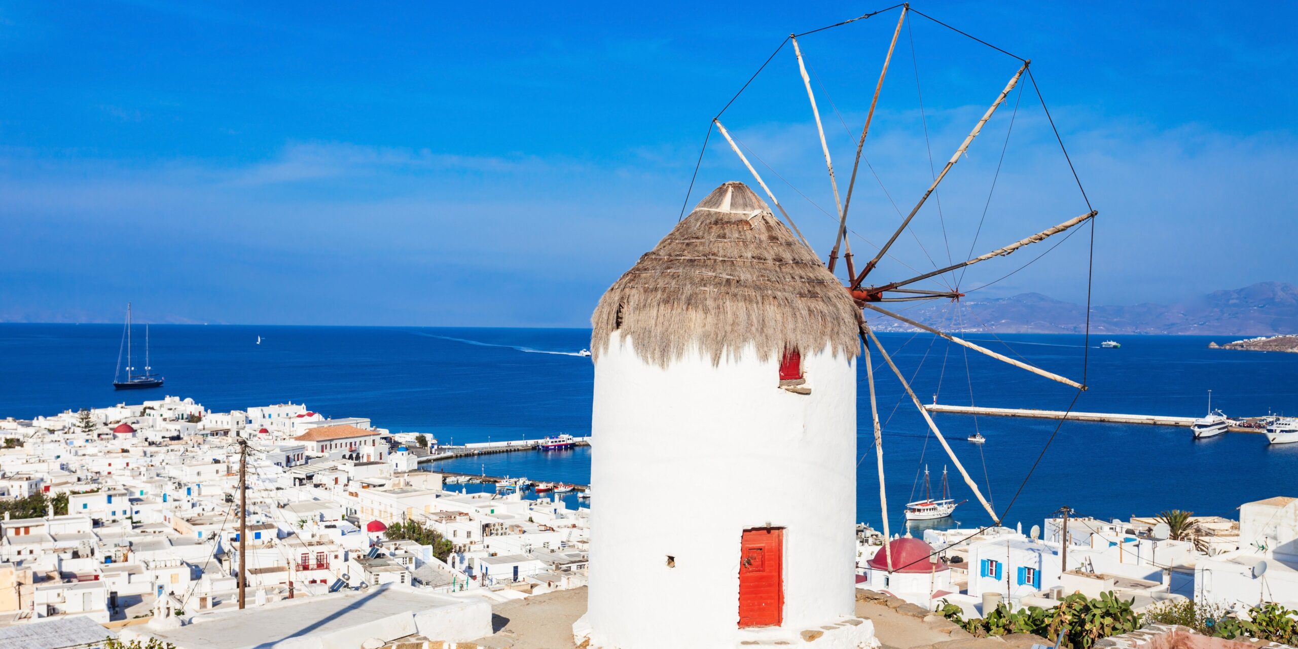 A traditional windmill overlooks the white buildings of Mykonos, with the blue sea stretching out to the horizon.