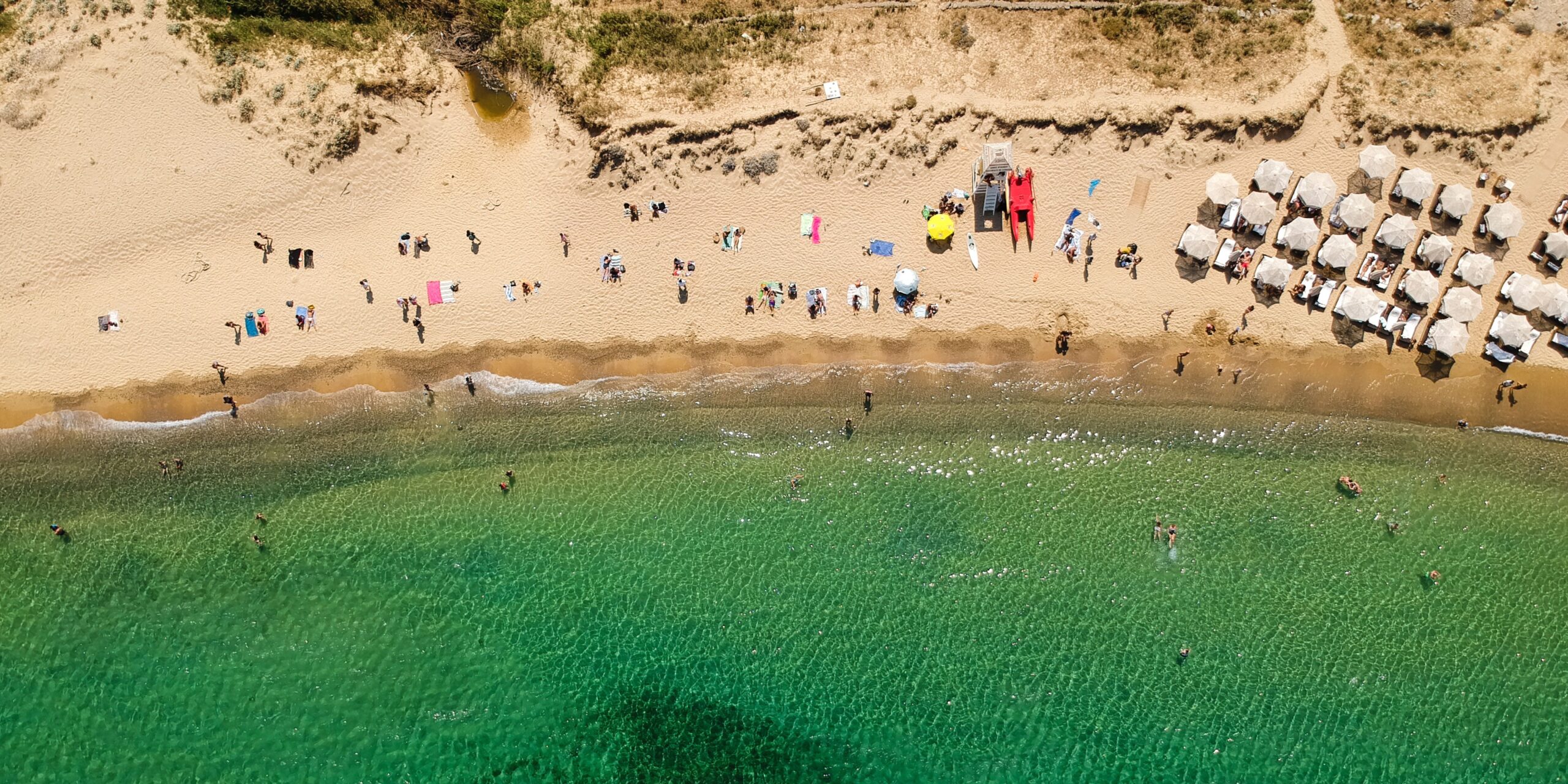 A lively scene at Panormos Beach where people are scattered across the sand, enjoying the sparkle of the sun on the water.