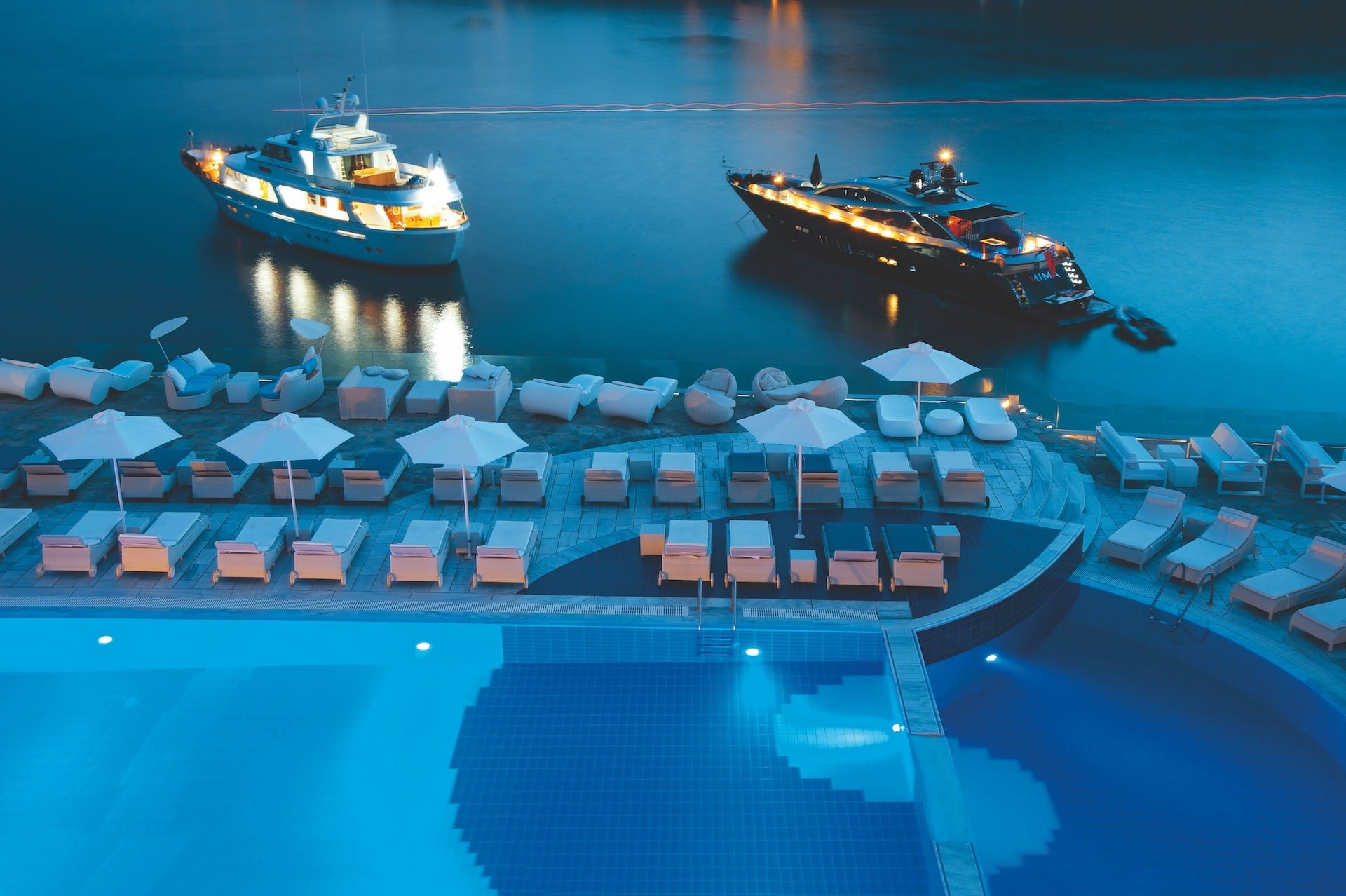 Tranquil poolside view at Petasos Hotel and spa in Mykonos, with boats adding a touch of romance under the starry sky.