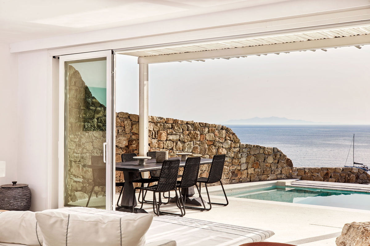 A photo of a living room with a table and chairs next to a swimming pool that overlooks the ocean.