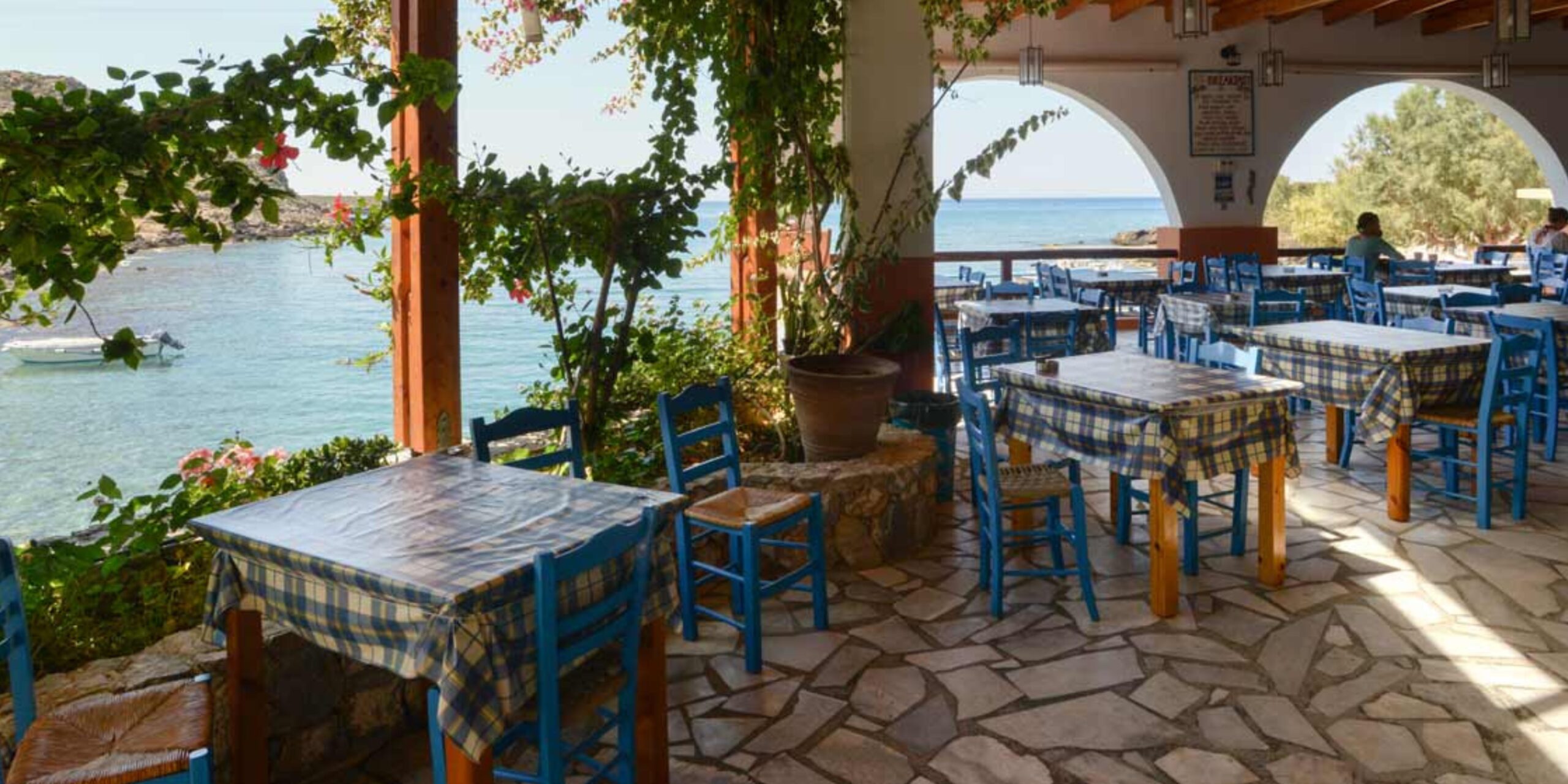 Seaside taverna with blue and white checked tablecloths and a view of the ocean.