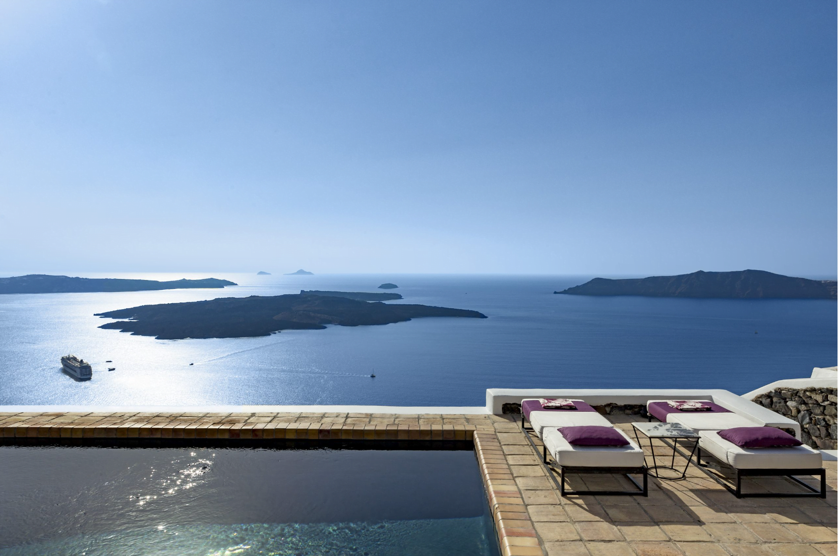 A tranquil poolside with sun loungers overlooking a panoramic view of the sea and distant islands.