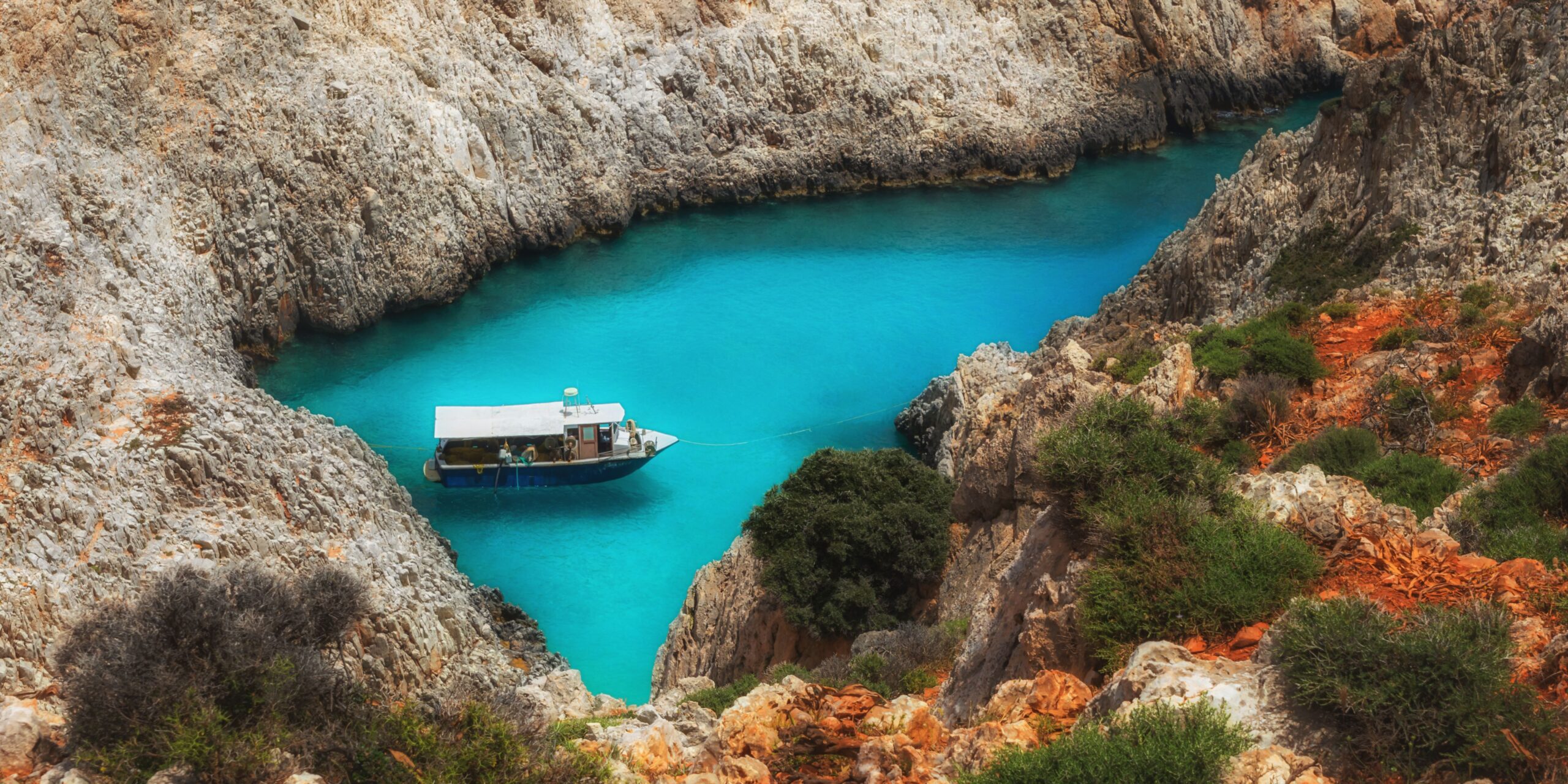 A boat anchored in a secluded blue cove surrounded by rugged cliffs.