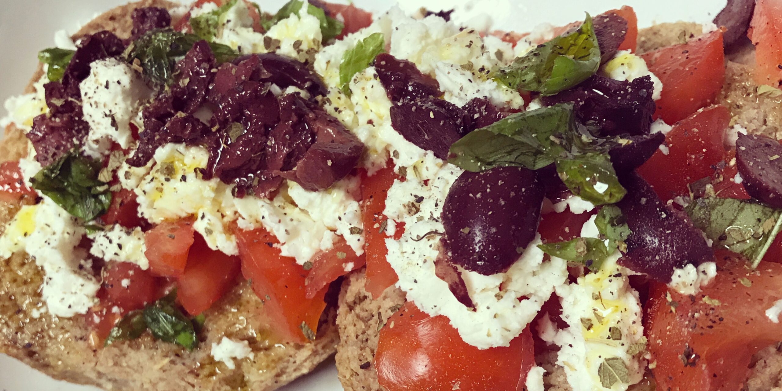Open-faced sandwich topped with tomatoes, cheese, olives, and herbs on a plate.