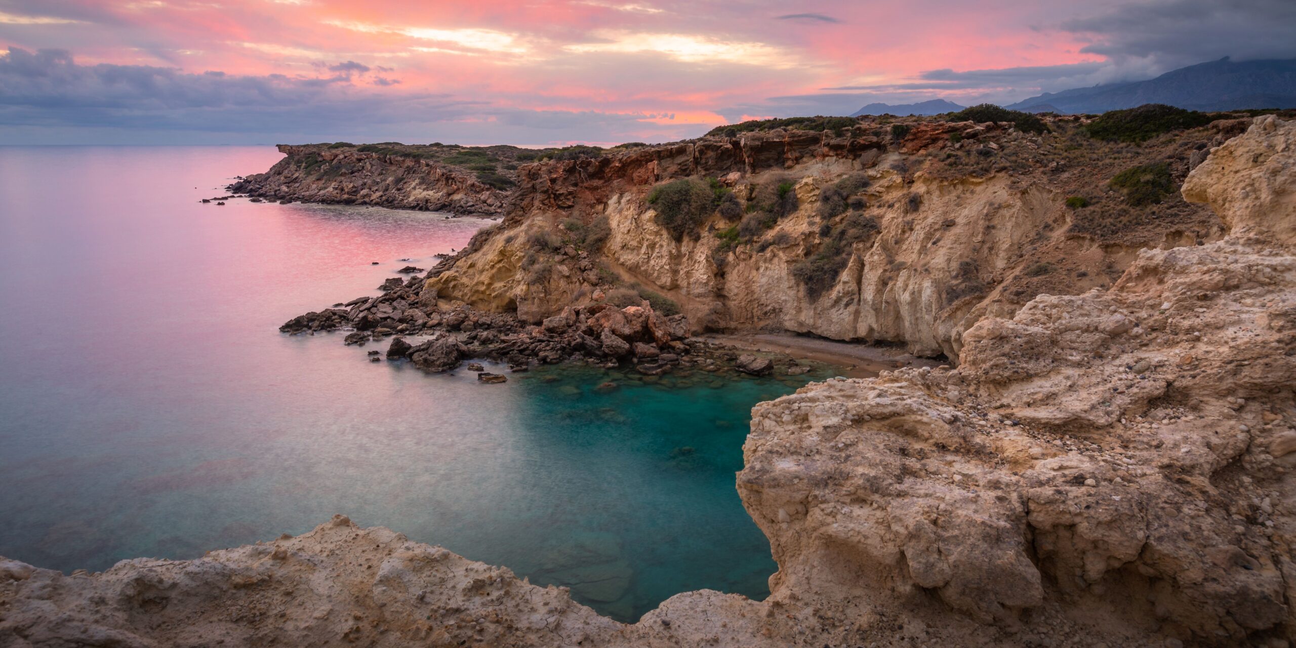 A serene cove with rocky cliffs and turquoise waters under a sunset sky.