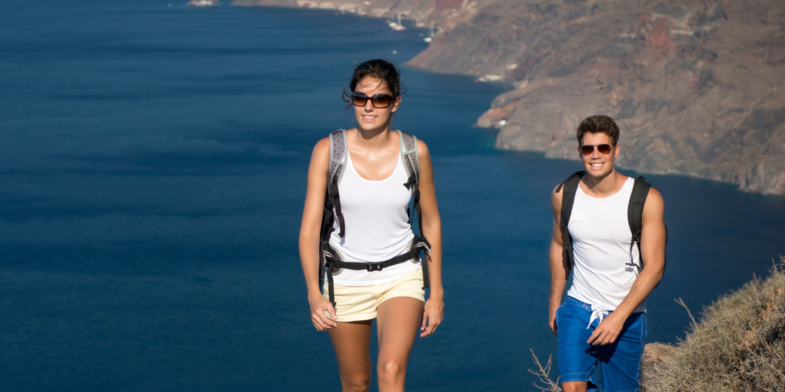 Two hikers with backpacks standing on a hill with the sea in the background.