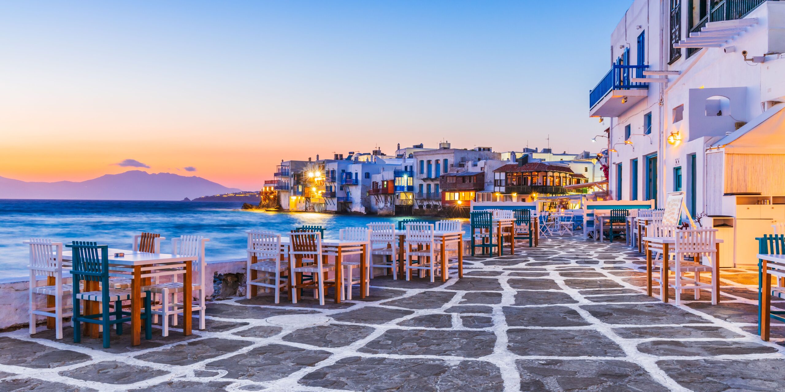 Evening falls on the charming seaside dining area in Little Venice, Mykonos, with tables set up for a beautiful night ahead.