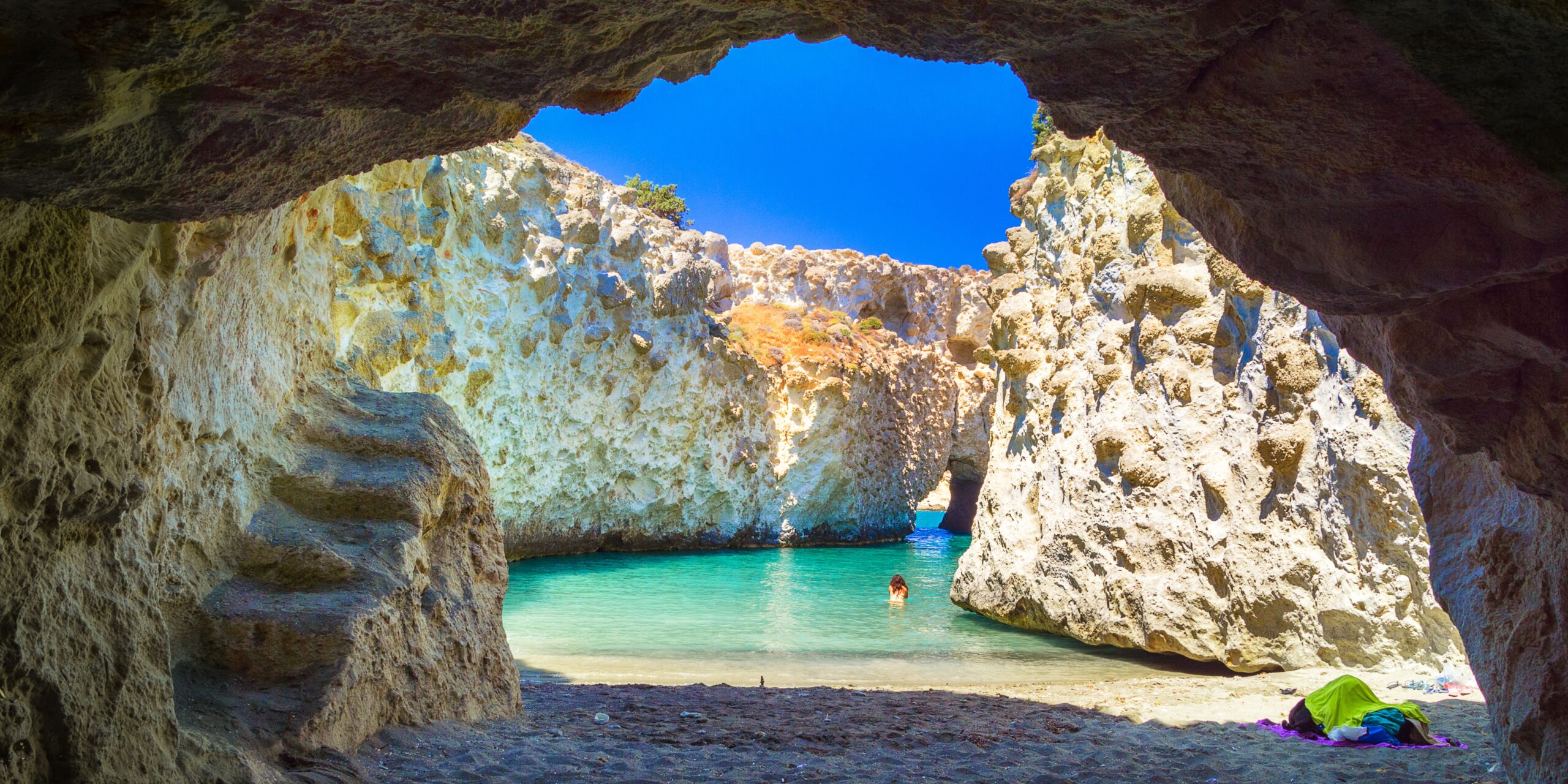 a secluded beach on milos island with only one woman swimming in the crystal clear waters