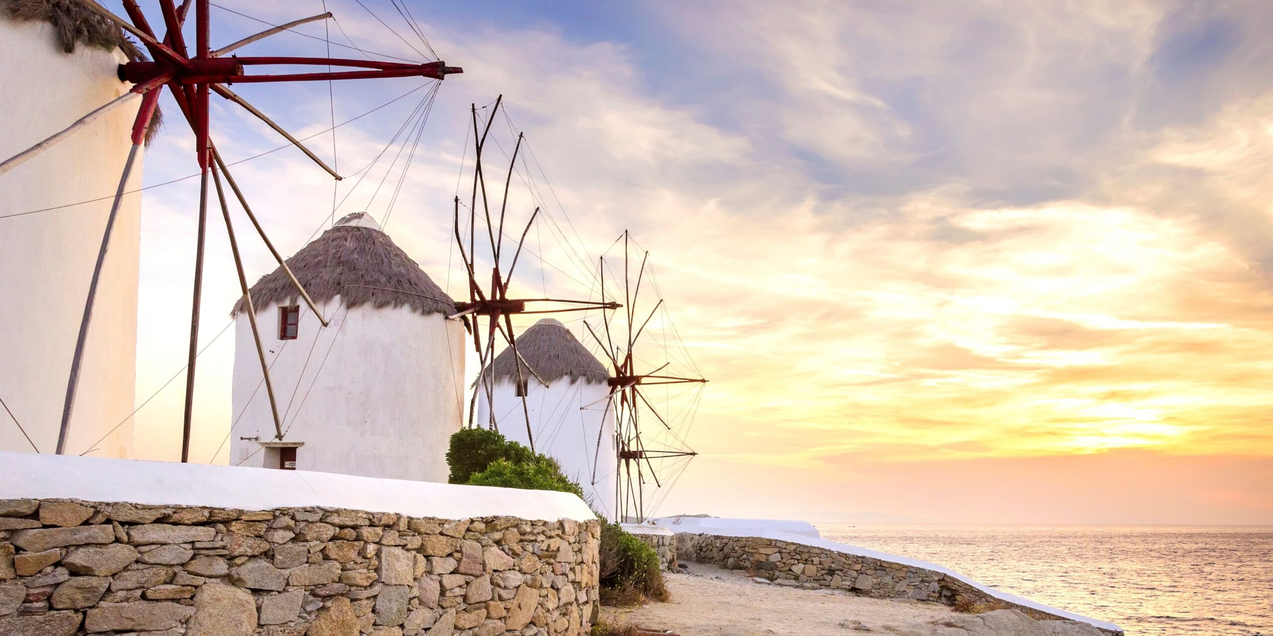 The iconic Mykonos windmills bask in the warm glow of the setting sun, creating a picture-perfect end to the day.