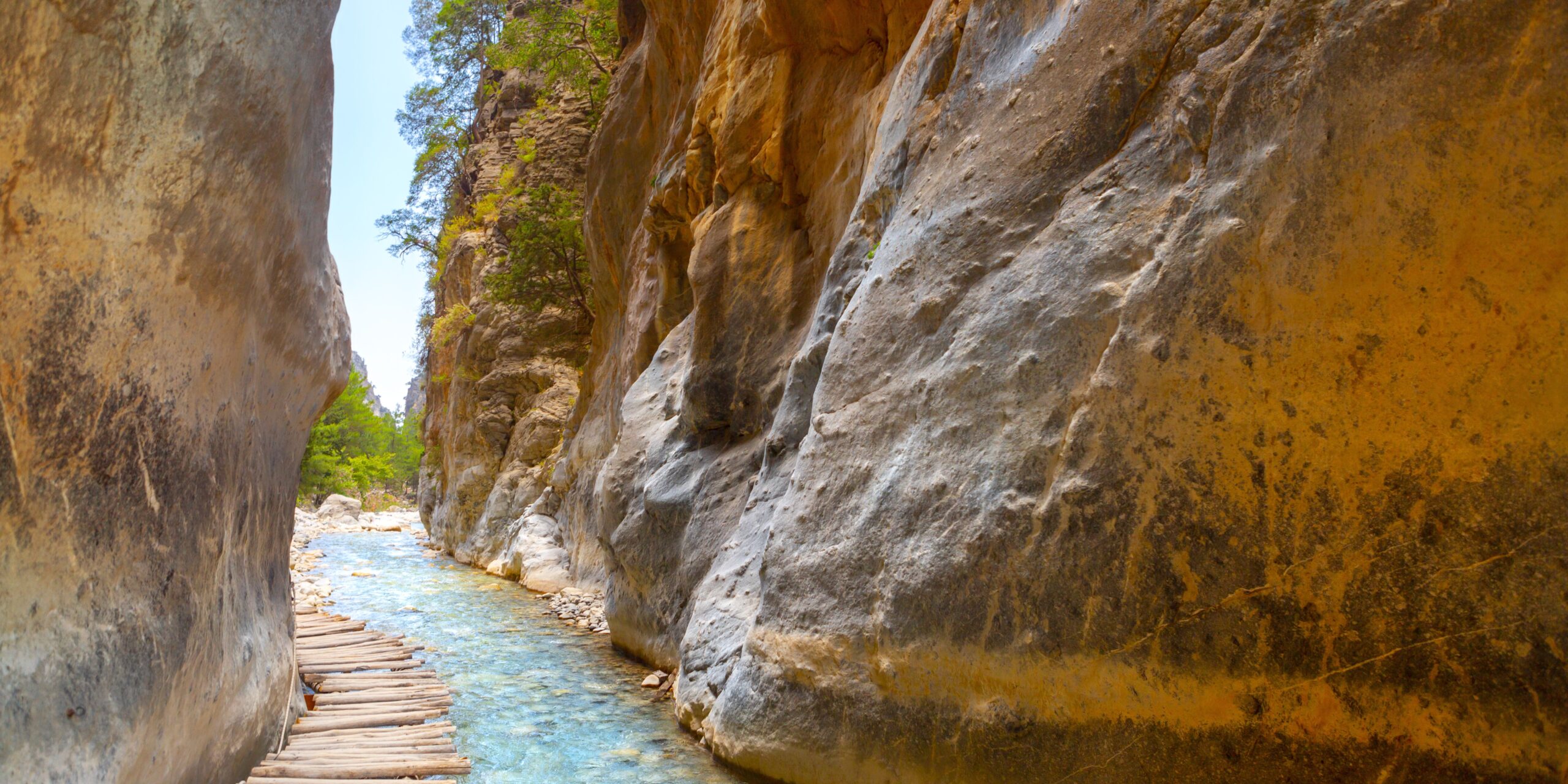 A wooden walkway running between tall, smooth rock walls beside a clear stream in a narrow gorge.