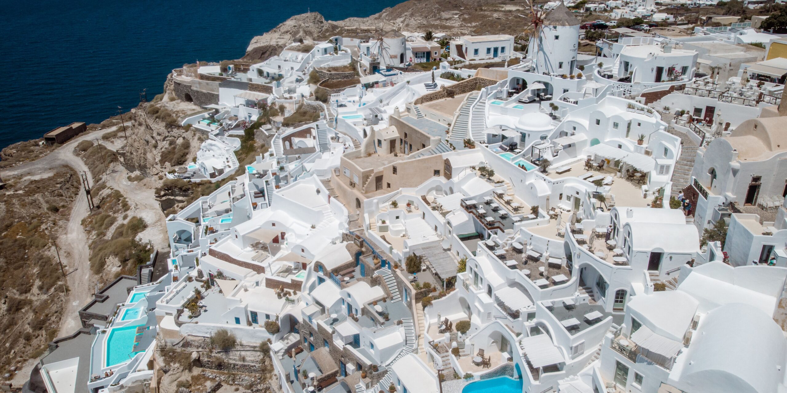 aerial view of santorini showing the hotels built on the cliff with a bunch of private pools