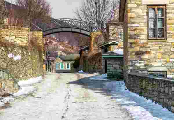A picturesque stone-paved street in Nymfaio, lined with stone houses and walls, with a light dusting of snow, creating a peaceful winter village scene. Nymfaio village_greece in winter_feature