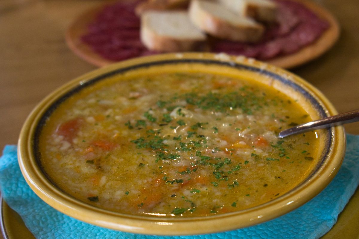 A bowl of traditional Greek trahana soup, garnished with herbs, served alongside sliced bread on a wooden table.