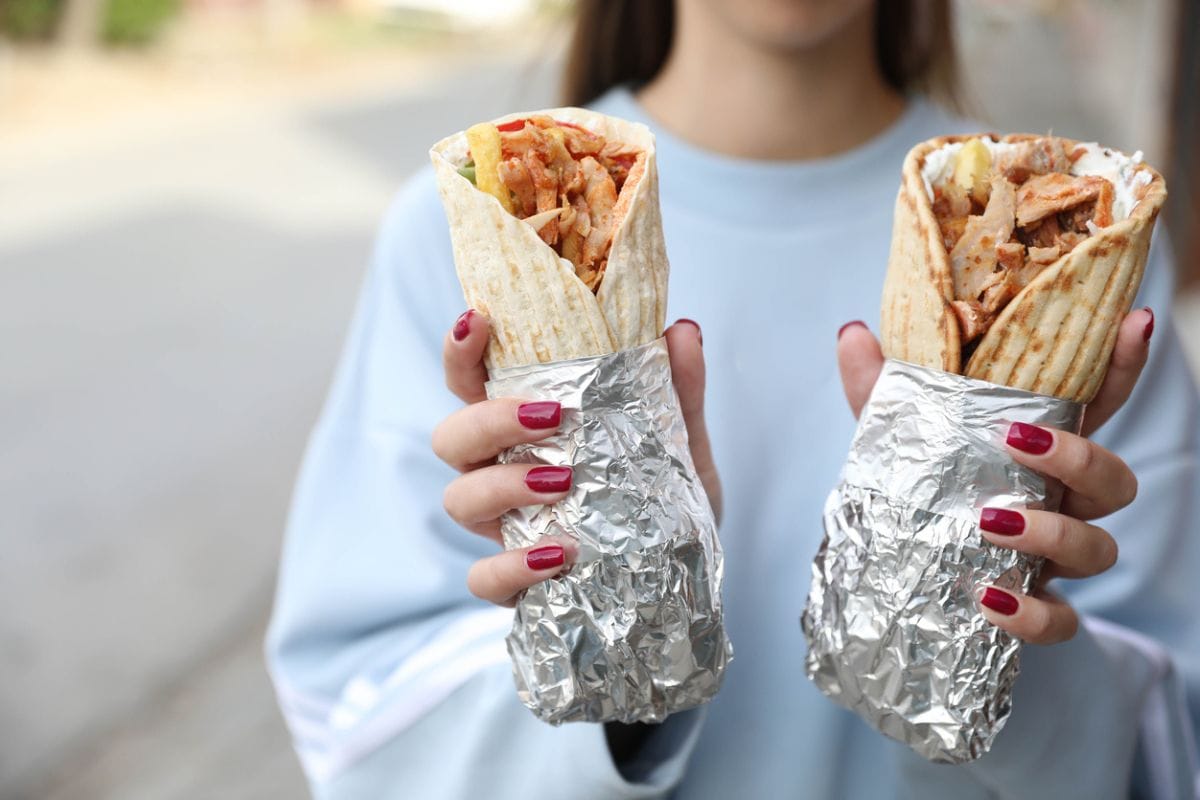 Unrecognizable person holding big juicy pita souvlaki with fries, tzatziki sauce and vegetables in close-up