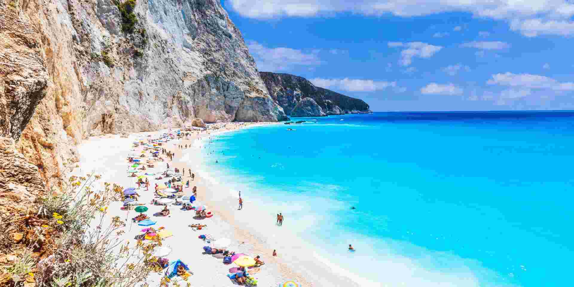 A stunning beach in Lefkada island in Greece with turquoise waters and white cliffs, filled with people enjoying the sun and sea. Lefkada_best greek islands to visit in september_feature