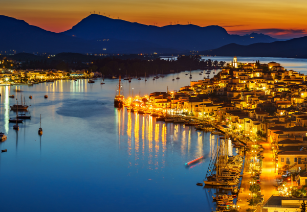A stunning evening view of Poros Island, featuring illuminated buildings along the waterfront, boats anchored in the calm waters, and mountains silhouetted against the colorful sunset sky. Poros island greece_feature
