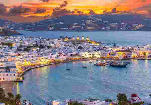 Embrace the warm hues of sunset in Mykonos Town Chora, where the Aegean Sea's azure waters reflect the vibrant life of this iconic Greek island. Mykonos travel_feature