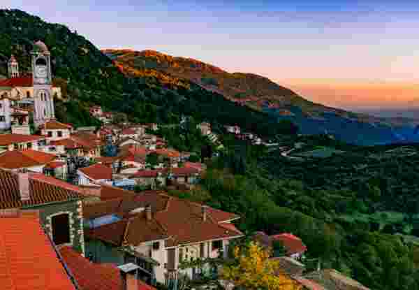 A breathtaking view of the sunset over Dimitsana, a picturesque mountain village in the Peloponnese region of Greece. The vibrant colors of the sky beautifully contrast with the serene landscape, capturing the tranquil essence of this charming village. Dimitsana Arcadia_Mountainous Villages in Greece_feature