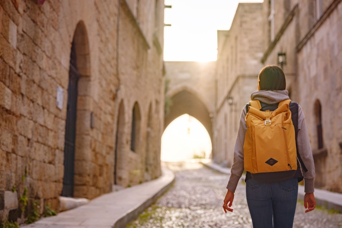 spring or fall trip to Rhodes island, Greece. Young Asian woman walks Street of Knights of Fortifications castle over sunset time. female traveler visiting southern Europe. Unesco world heritage site.