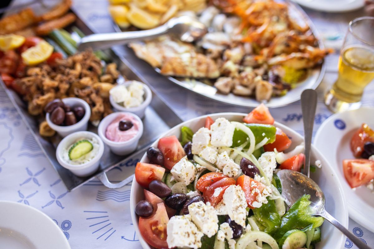 Greek salad, fresh vegetables, feta cheese and black olives in bowl and seafood on table