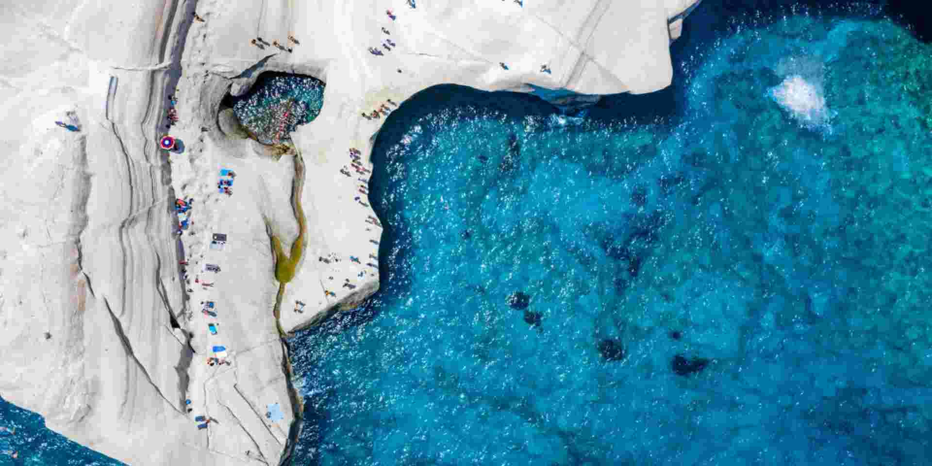Aerial view to the chalk rock formations of Sarakiniko with people enjoying the sparkling blue sea on a hot summer day, Milos island, Cyclades, Greece_Greek islands july Sarakiniko Milos island_Greek islands july_feature