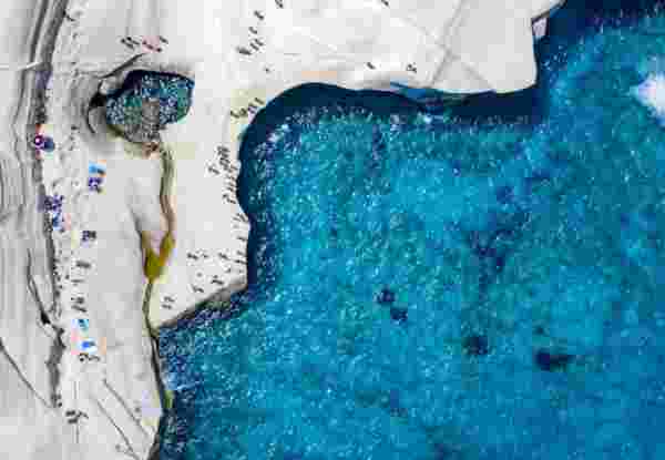 Aerial view to the chalk rock formations of Sarakiniko with people enjoying the sparkling blue sea on a hot summer day, Milos island, Cyclades, Greece_Greek islands july Sarakiniko Milos island_Greek islands july_feature
