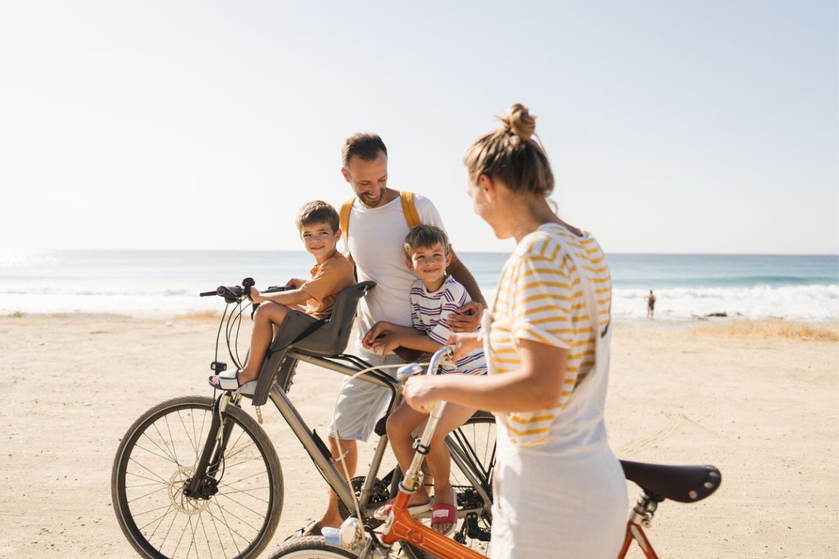Photo of a young family, with two little boys, enjoy beautiful summer morning riding bicycles by the sea