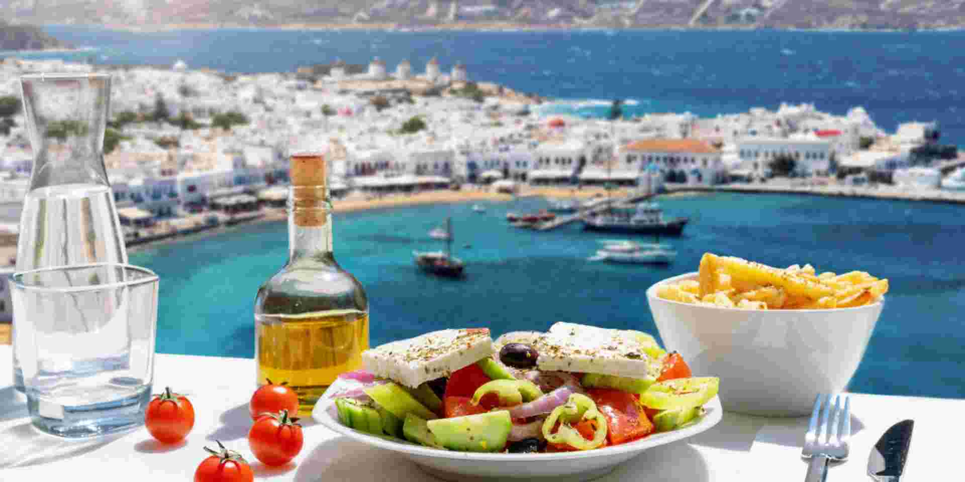 Tasty Greek food with salad, feta cheese and olive oil served with a view to the beautiful island of Mykonos, Greece, during summer time Mykonos restaurants_feature