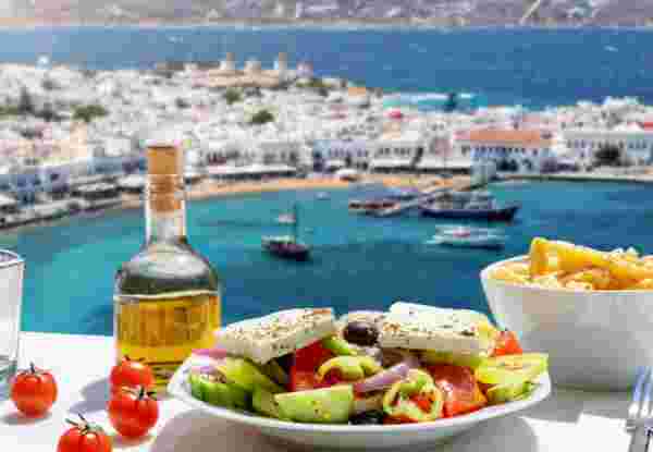 Tasty Greek food with salad, feta cheese and olive oil served with a view to the beautiful island of Mykonos, Greece, during summer time Mykonos restaurants_feature