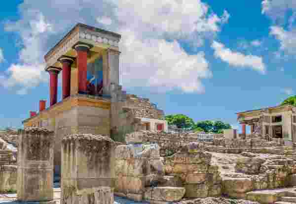 A partially restored section of the Knossos Palace complex, featuring red columns and stone ruins under a bright sky. knossos palace_historical sites in Greece_feature
