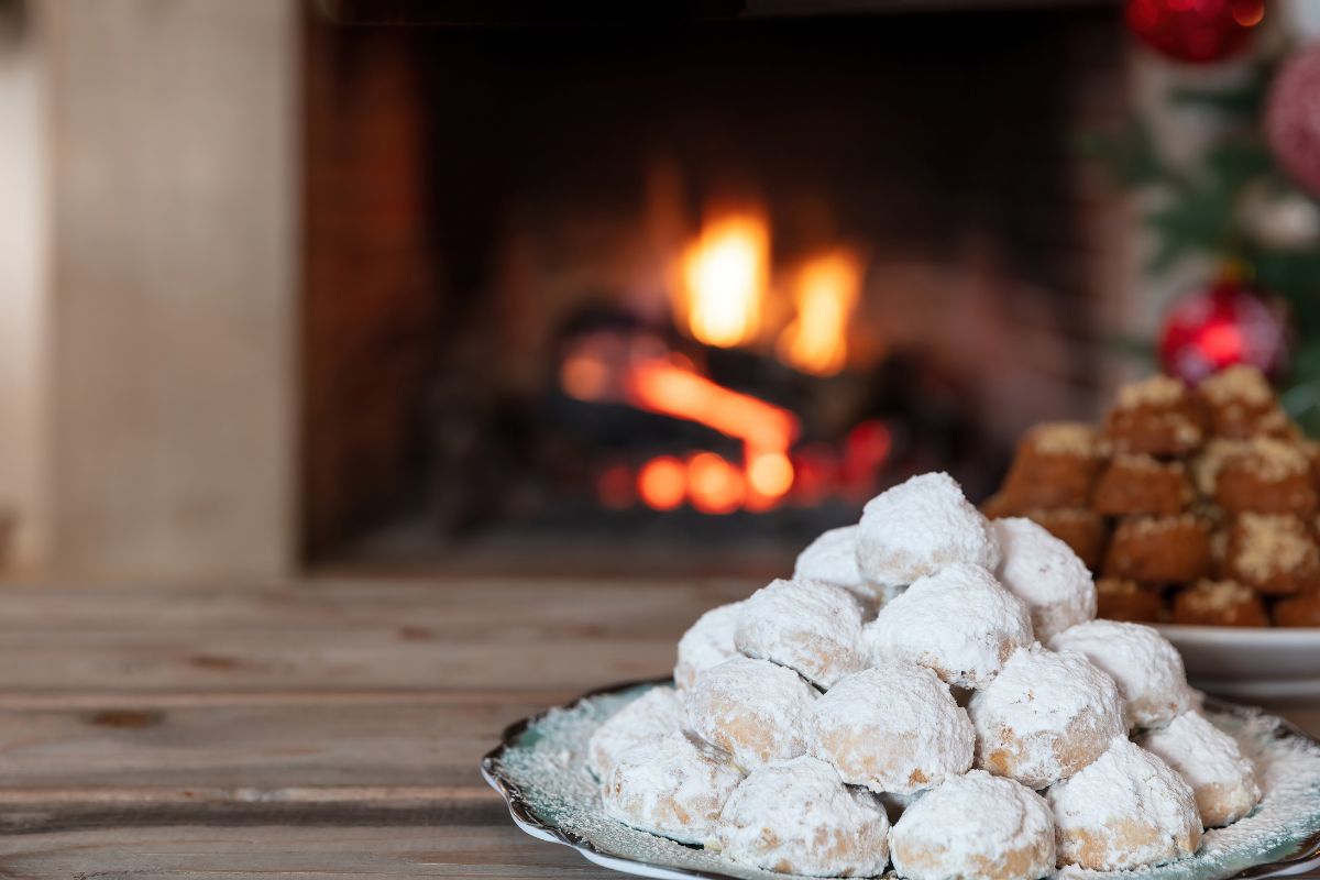 A plate of kourabiedes and melomakarona, traditional Greek Christmas cookies, dusted with powdered sugar and drizzled with honey in the background.