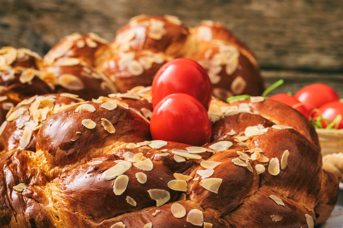 A close-up of tsoureki, a Greek sweet bread, topped with almond slices and decorated with red eggs.
