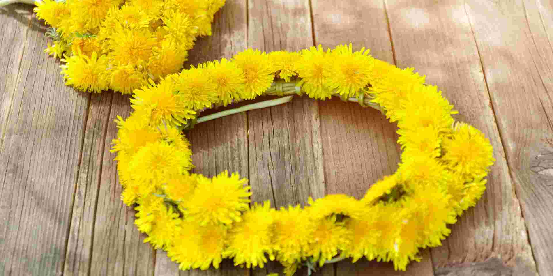 Handmade May Day flower wreath with yellow dandelions placed on a wooden surface. may first greece_feature