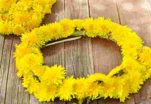 Handmade May Day flower wreath with yellow dandelions placed on a wooden surface. may first greece_feature