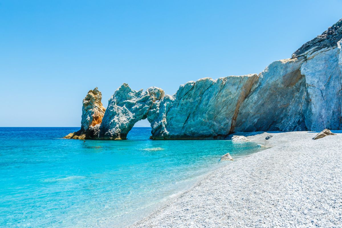 Lalaria Beach in Skiathos features clear blue water, a distinctive rock arch, and a pristine pebble shore.