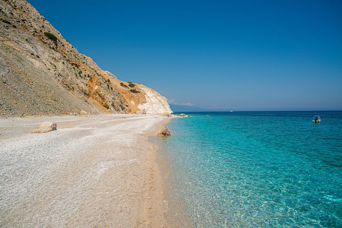 A beach in Skiathos with clear blue water, a pebble shore, and rocky cliffs in the background. 