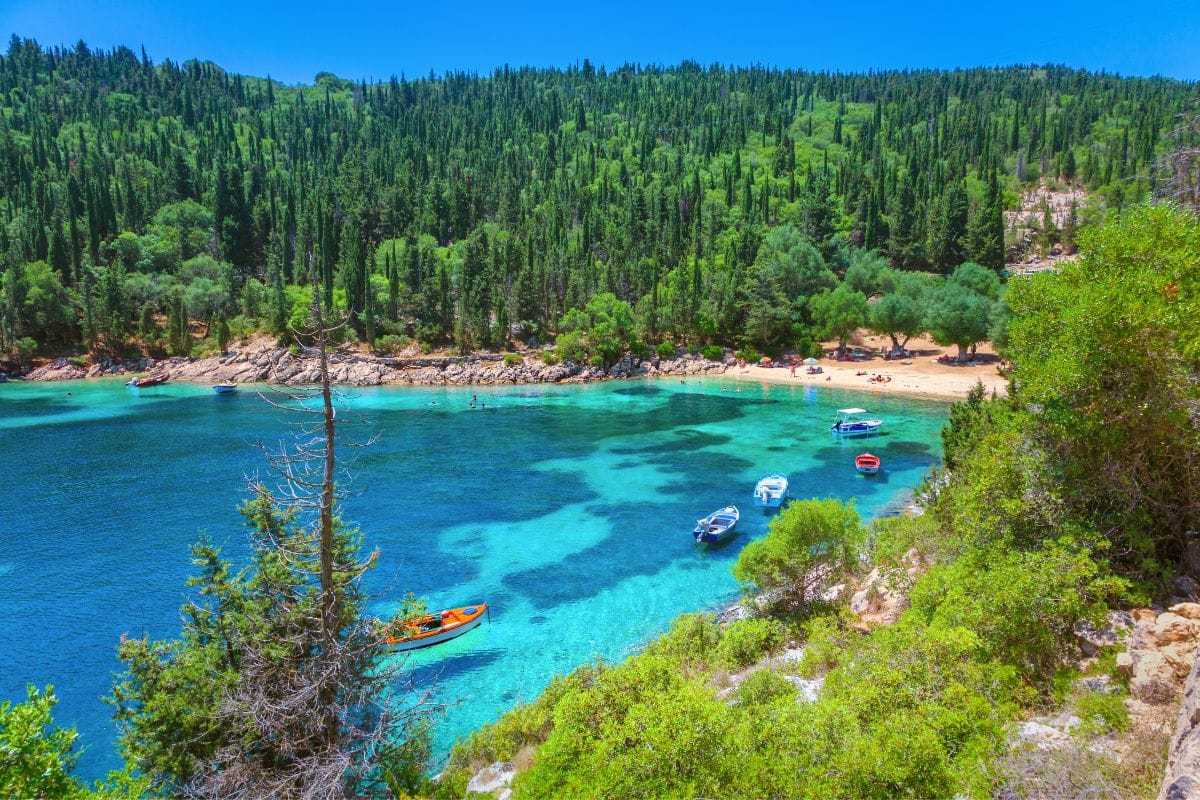 A beautiful view of Fiskardo in Kefalonia, featuring clear turquoise waters, small boats, and a lush green forest surrounding the bay.