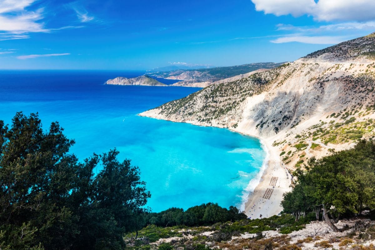 A scenic view of Myrtos Beach in Kefalonia, showcasing the vibrant turquoise waters, white sandy shore, and surrounding cliffs.