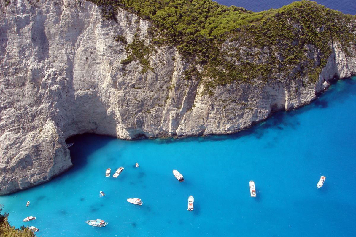 Aerial view of Zakynthos Island’s iconic cliffside and crystal-clear blue waters, with small boats scattered along the shoreline.