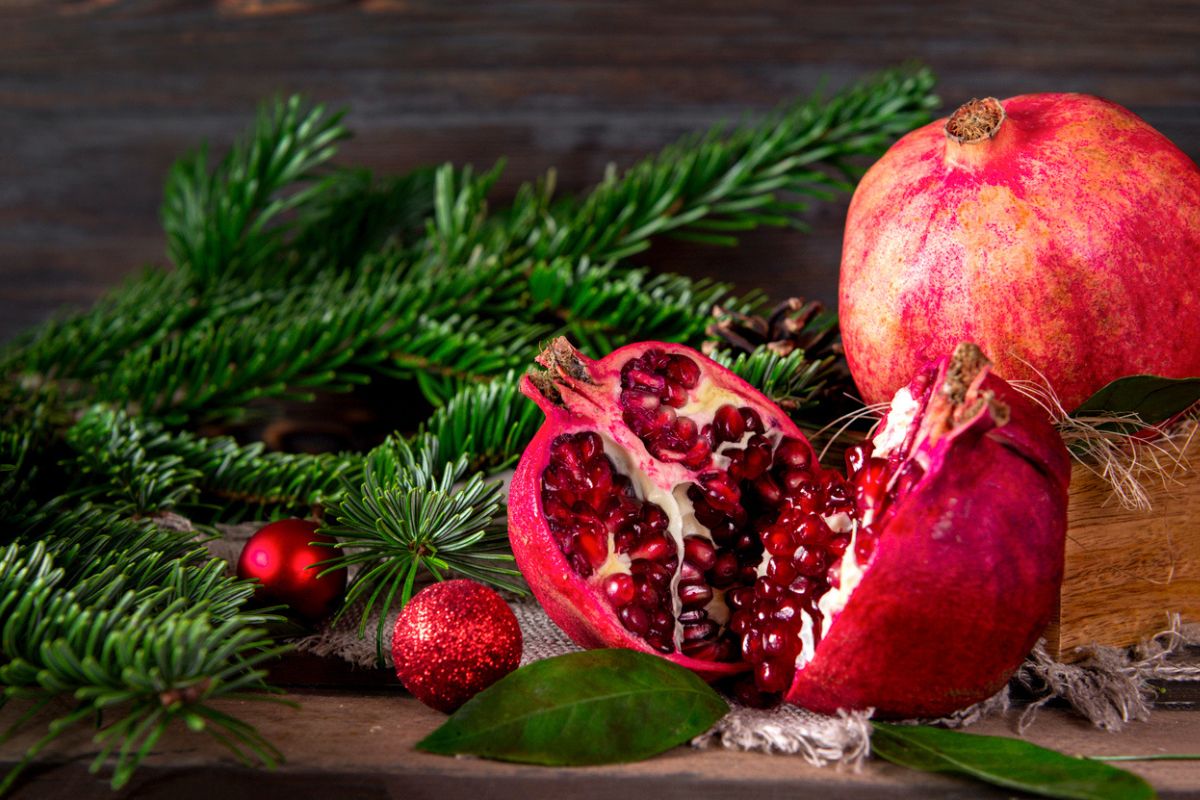 red ripe pomegranate, fir branches, red Christmas balls on a dark wooden background