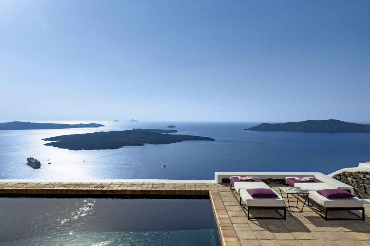 A tranquil poolside with sun loungers overlooking a panoramic view of the sea and distant islands.