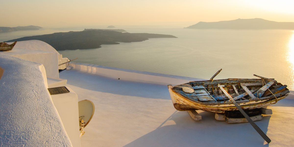 Old wooden boat on a white rooftop overlooking the sea at sunset.