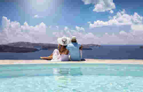 A elegant couple in summer clothes sits by the pool and enjoys the view to the mediterranean sea