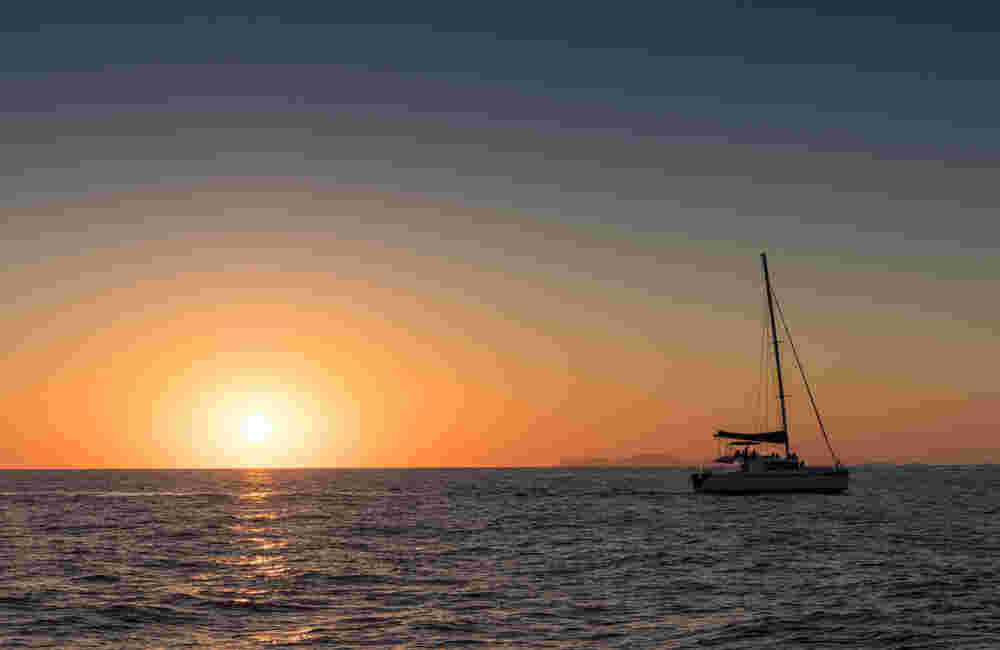 Beautiful sunset in Oia, Santorini, seen from the sea with silhouette of catamaran.