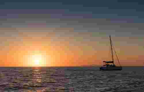 Beautiful sunset in Oia, Santorini, seen from the sea with silhouette of catamaran.