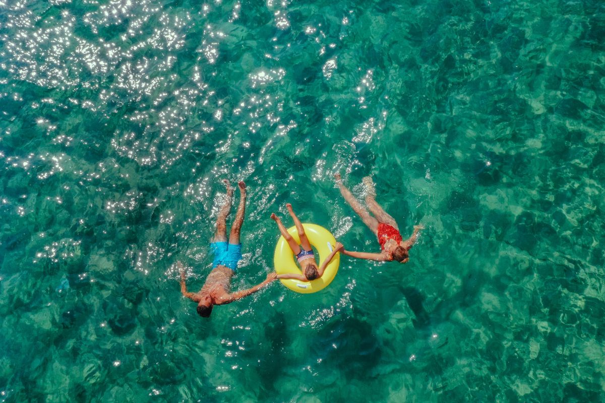 mom, dad and child in the sea and the child is on a floaty in Greece and they are all holding hands